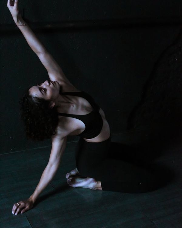 Woman in a dynamic yoga pose against a dark background.